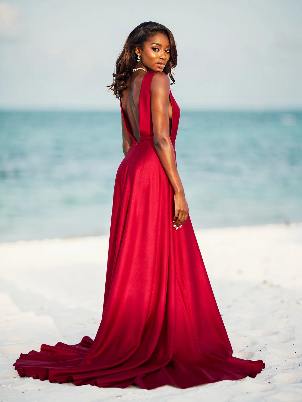 A woman in a low-back rose-red gown with a long train on white sand