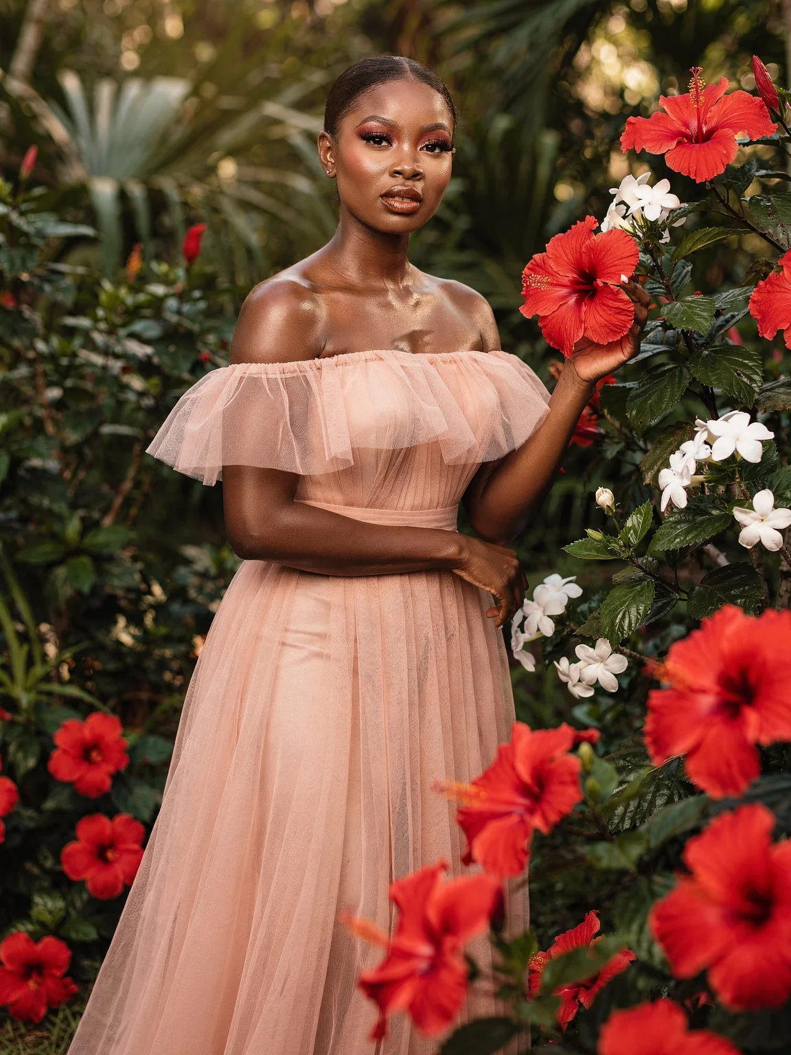 A woman in a blush tulle gown among red hibiscus flowers