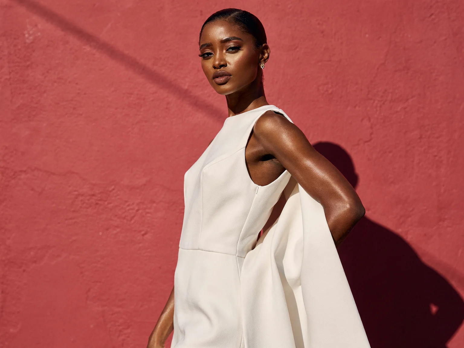 A woman in a white structured gown against a flat rose-red wall